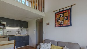 Ein zeitgemäßer Wohnraum mit grauem Sofa, gemusterten Kissen, einer Küchenzeile mit dunklen Schränken und einem dekorativen Wandbild.