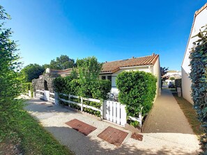 A residential property with a paved driveway, white fence, and a well-maintained garden.