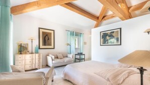 Quarto com uma cama grande, cômoda, cadeira e escrivaninha. Há duas pinturas nas paredes.