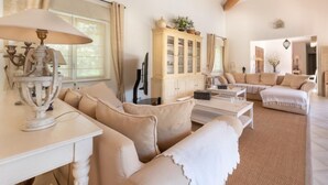 Uma sala de estar ampla, com um sofá branco, uma mesa de centro de madeira e um armário com portas de vidro.