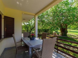 Une terrasse couverte avec une table et des chaises, un pot de fleurs et une vue sur un jardin luxuriant.
