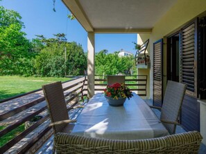 Une terrasse couverte avec une table, deux chaises en osier et un vase à fleurs.
