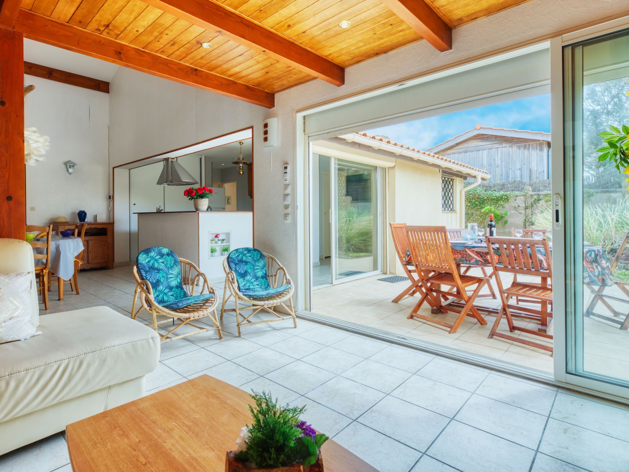 A spacious living area with a large sliding glass door leading to an outdoor patio. Inside, there is a sofa, two wicker chairs with blue cushions, and a wooden coffee table.