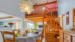 Un comedor con mesa y sillas de madera, una escalera a un nivel superior y vistas al exterior.