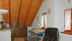 Une cuisine chaleureuse avec des poutres en bois, un coin repas avec une table et des chaises, et un fauteuil en cuir noir.