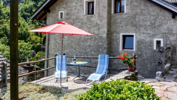 Un bâtiment en pierre doté d’un balcon, deux chaises bleues, un parasol rouge et une table.