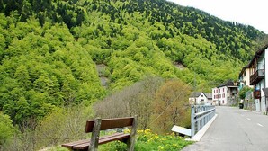 Un banc au bord d’une route, avec une montagne en arrière-plan et des maisons.