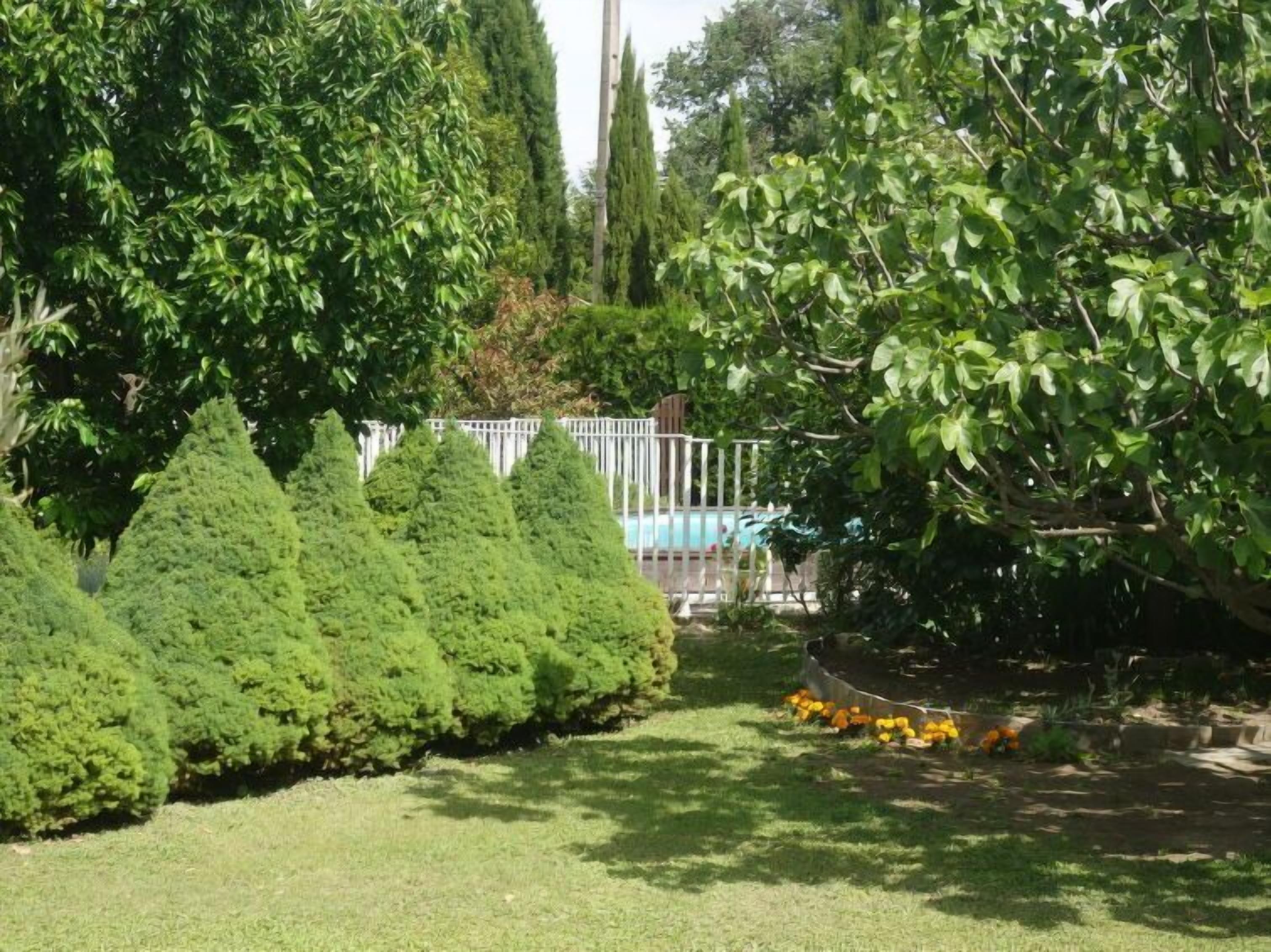 A well-maintained garden with neatly trimmed hedges, a white fence, and a pool area.