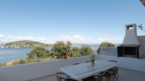 Une terrasse avec une table et des chaises donnant sur un plan d’eau et des collines.