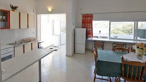 Une cuisine moderne avec des meubles blancs, une table à manger avec des chaises et une grande fenêtre donnant sur un paysage verdoyant.