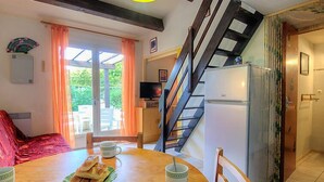 Uma área de refeições com mesa de madeira, cadeiras e um buffet de pães e uma chávena. Uma escadaria leva a uma cozinha com frigorífico.
