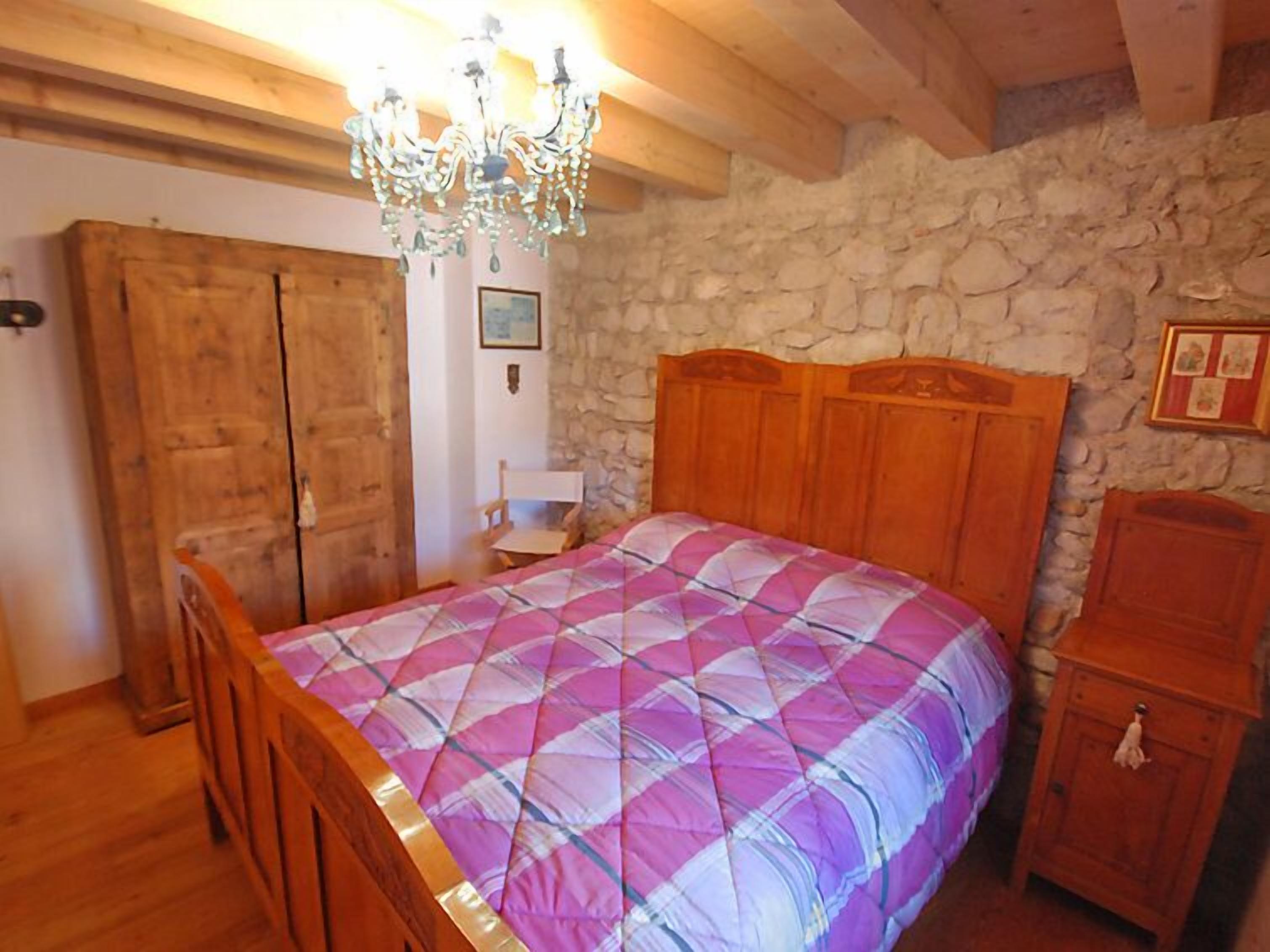 Un dormitorio con cama de madera, pared de piedra y armario de madera.