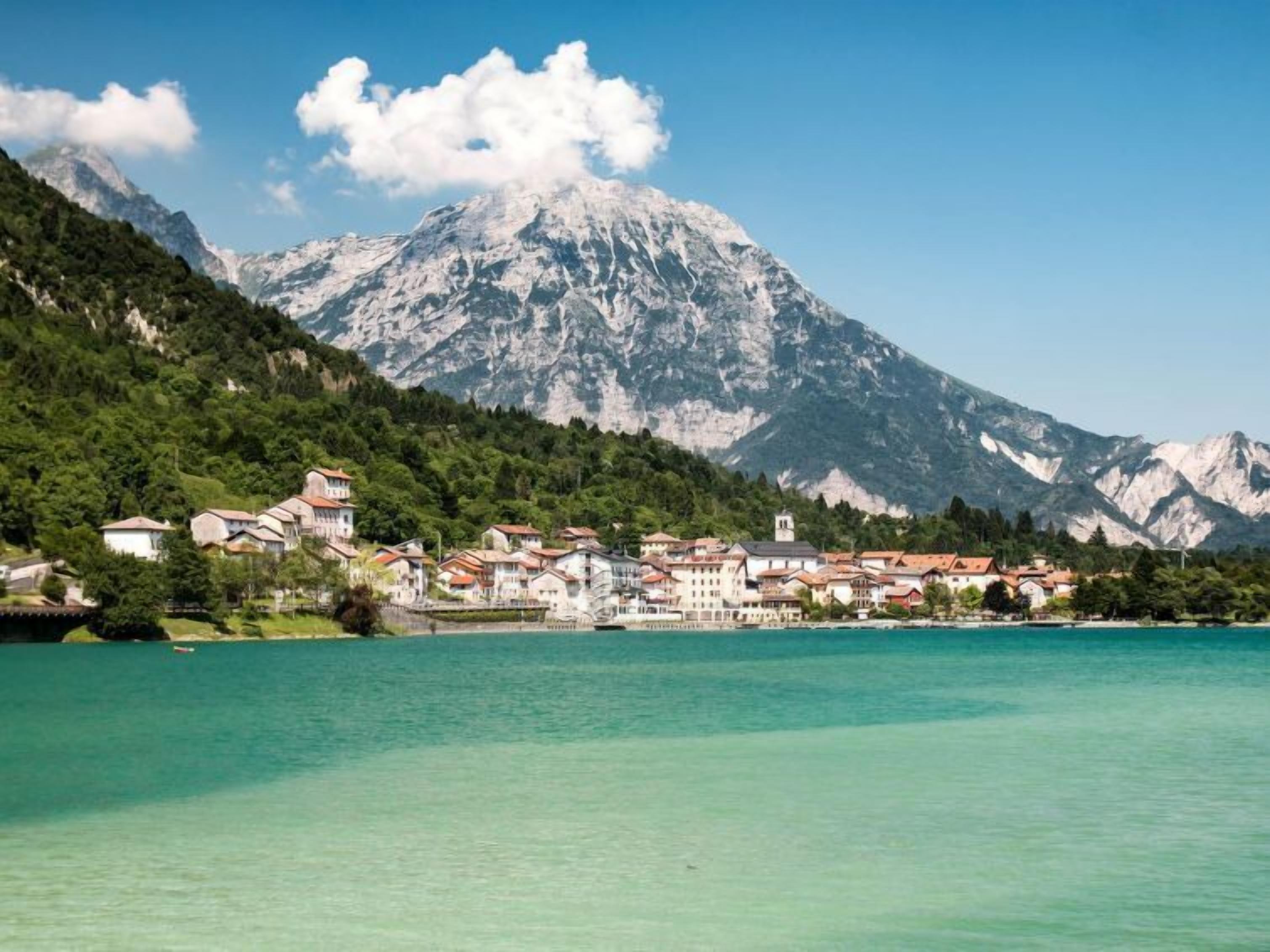A coastal town with buildings along the waterfront, a mountain in the background, and clear turquoise water.