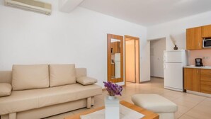 A modern living room with a beige sofa, a wooden coffee table, and a small white table with a vase of purple flowers. - Apartment Mare 8 by Interhome (Rab/Kampor)