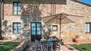A stone building with a patio area featuring a table and chairs, a large umbrella, and potted plants. - Apartment Giotto by Interhome (Montaione)