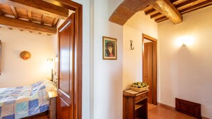 A room with a bed, a wooden door, a wall-mounted light, a framed picture, and a small table with a basket. - Apartment Giotto by Interhome (Montaione)