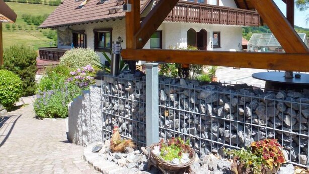Een klassiek chalet met een stenen muur, een houten balkon en uitzicht op een groene vallei.