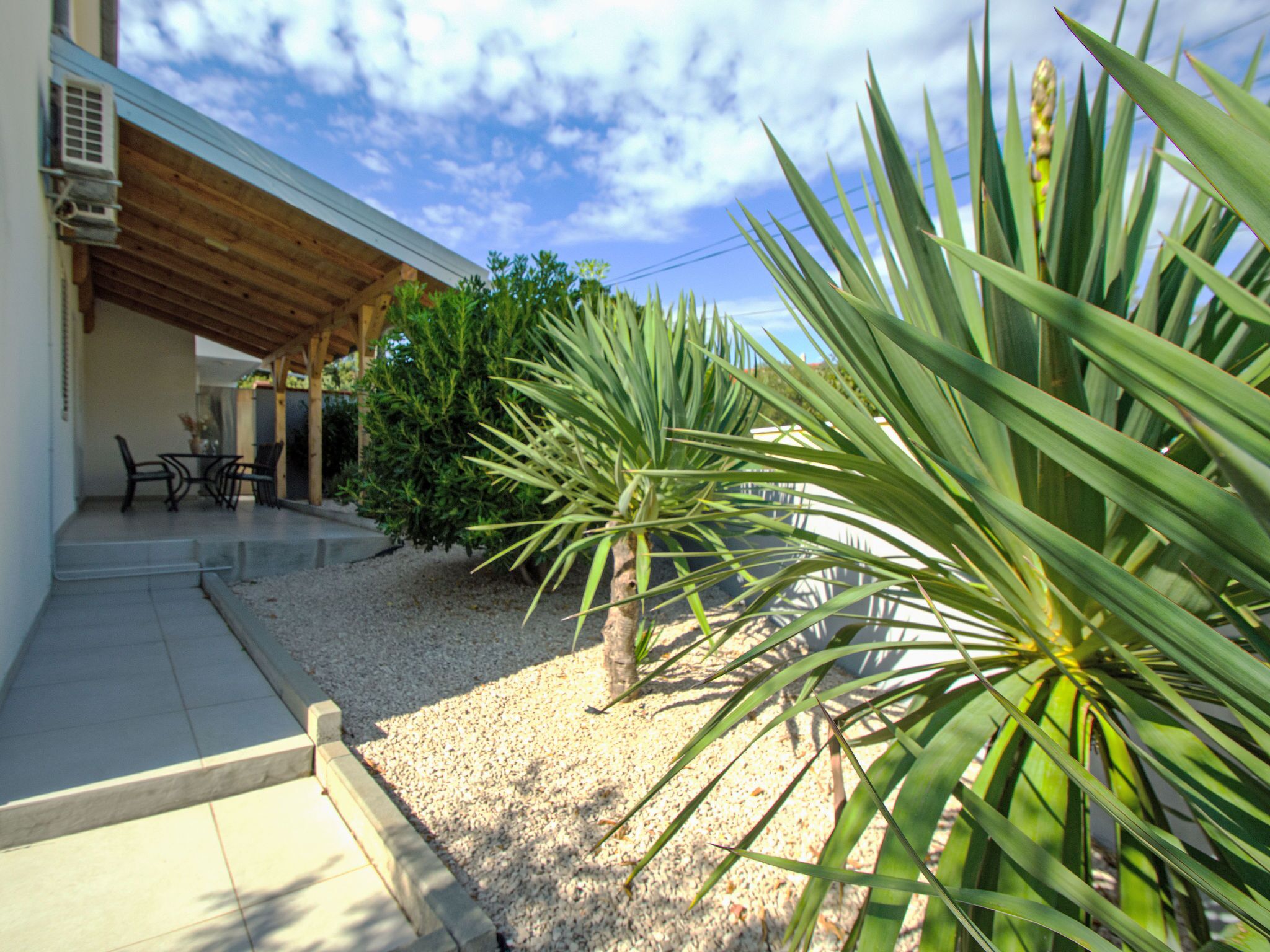 Un patio techado con mobiliario exterior y diversas plantas.