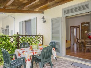 Eine Terrasse im Freien mit Esstisch und Stühlen, unter einem Holzbalkenüberdachung.