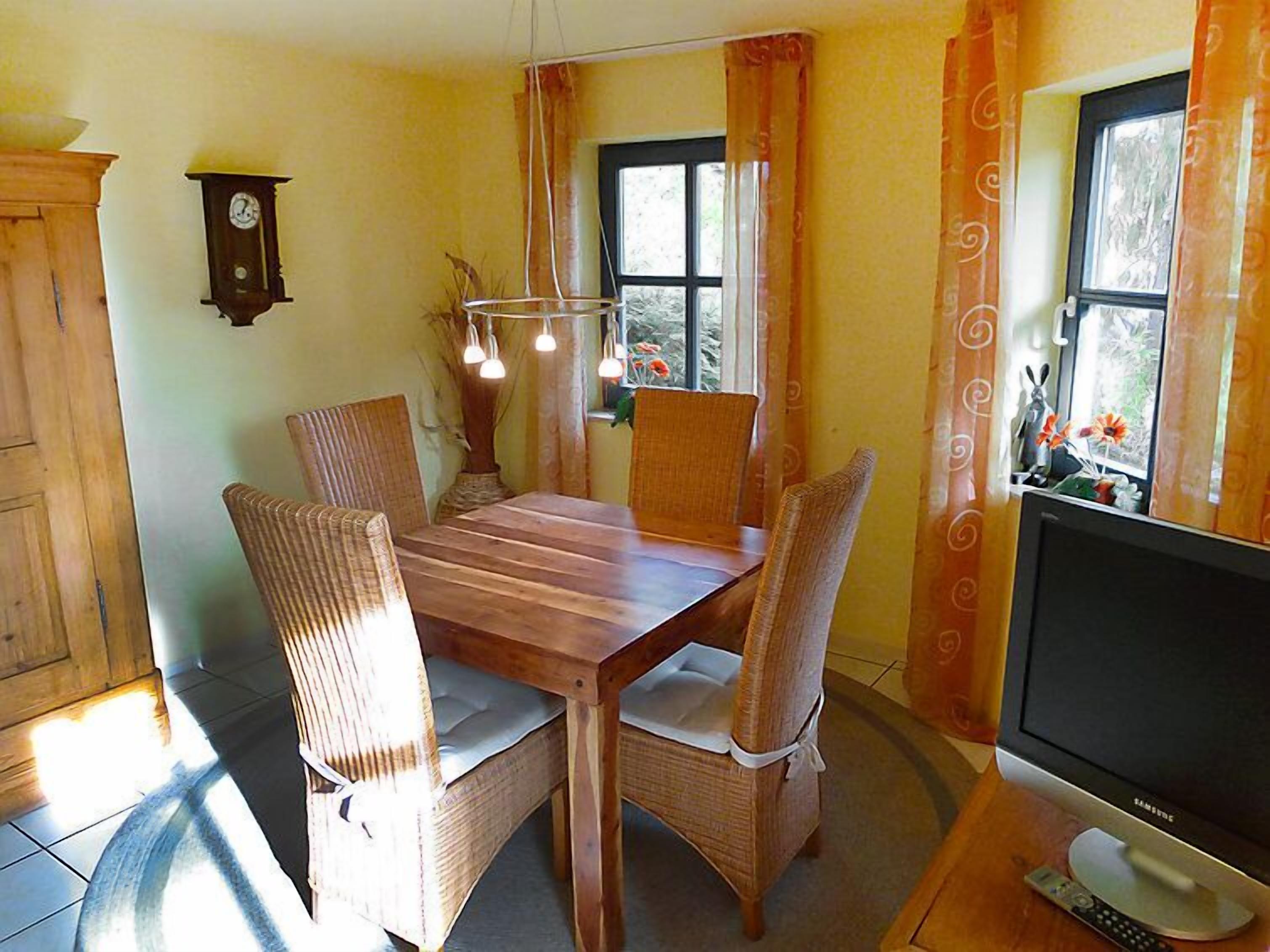 Un comedor con una mesa de madera, sillas de mimbre, un reloj de pared y un televisor.