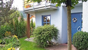 Un edificio a due piani con una porta e una finestra blu, immerso in un giardino curato e ricco di piante e fiori.