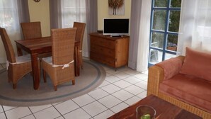 Zona pranzo con tavolo e sedie in legno, TV su mobiletto in legno e divano nella zona soggiorno.
