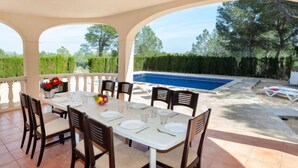 A covered outdoor dining area with a pool in the background. - Villa Alguer by Interhome (L'Ametlla de Mar)