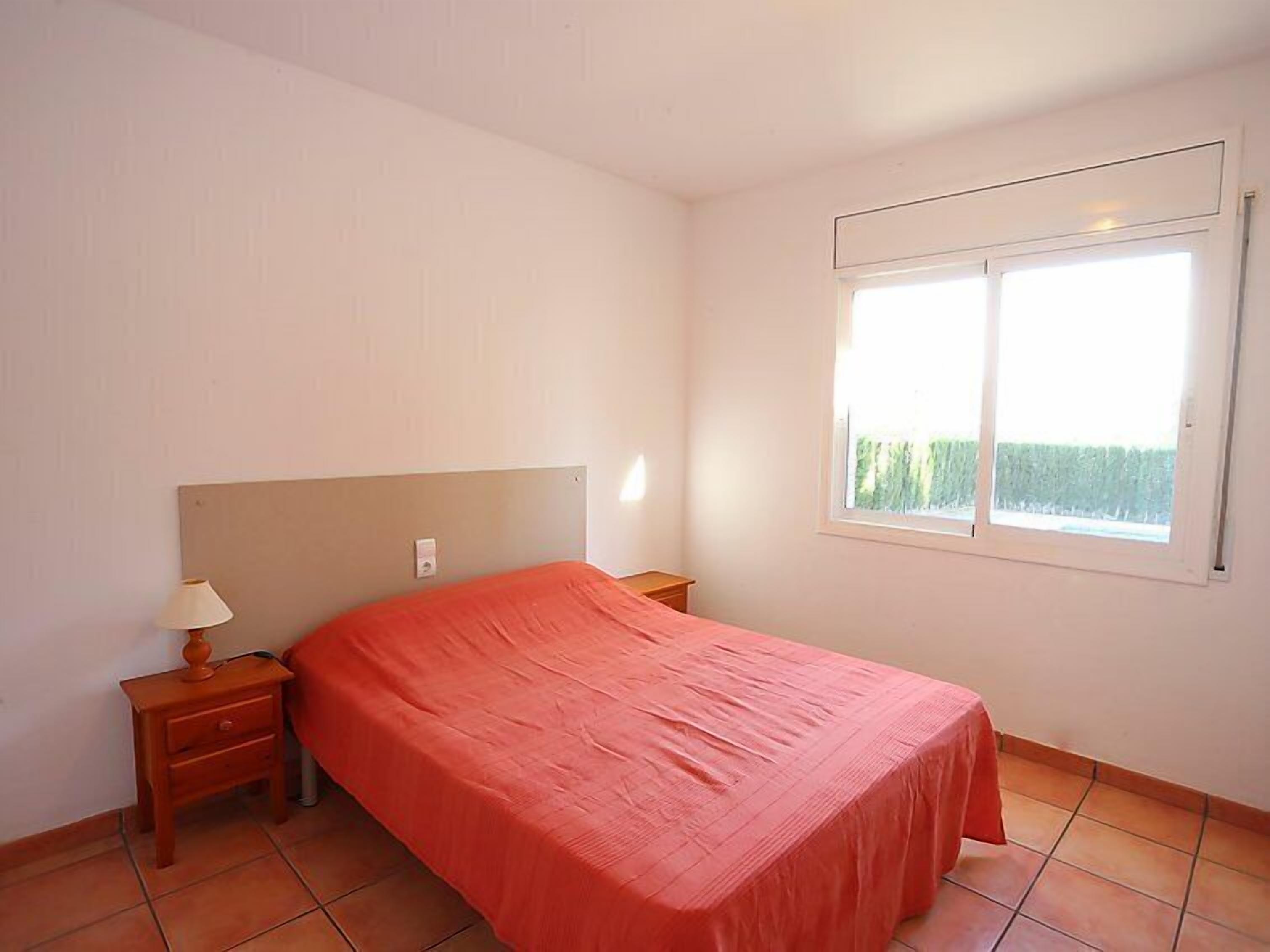 Un dormitorio con cama, mesita de noche, lámpara y ventana con vista a zonas verdes.