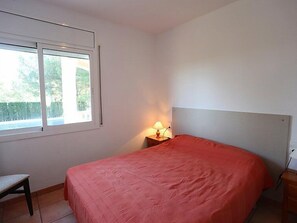 Una camera da letto con un letto, un comodino, una lampada, una sedia e una finestra vista alberi.