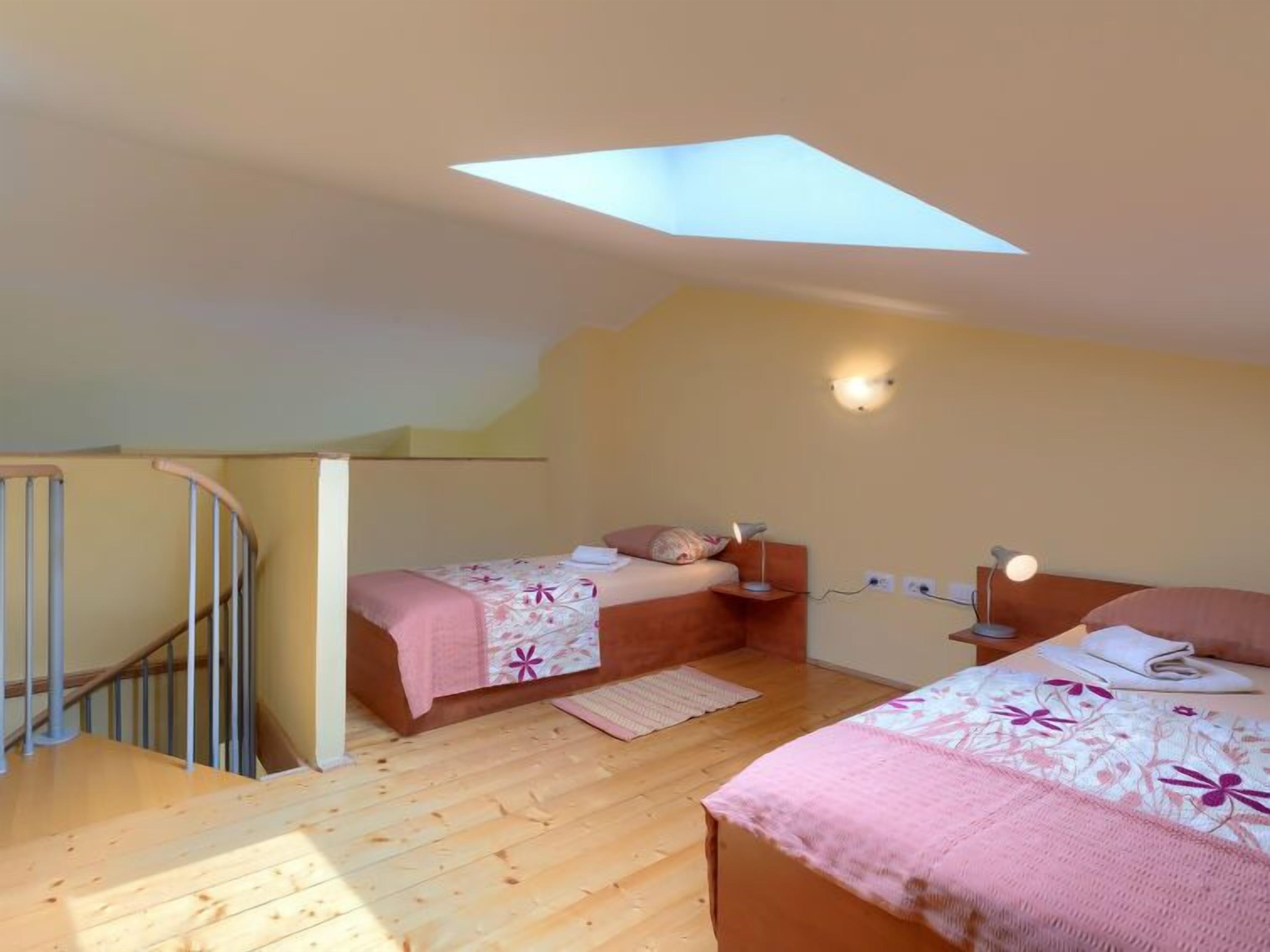 A bedroom with two beds, a skylight, a wooden staircase, and a wall-mounted light fixture.