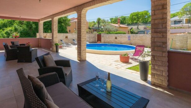 Un espace extérieur abrité comprenant une piscine, des chaises longues et une table avec des verres et une bouteille.