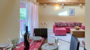 Un coin repas avec une table dressée pour deux personnes, un canapé rose et un tableau encadré au mur.
