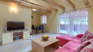 Un salon avec une télévision, un canapé rose, une table basse en bois et, au fond, un coin repas.