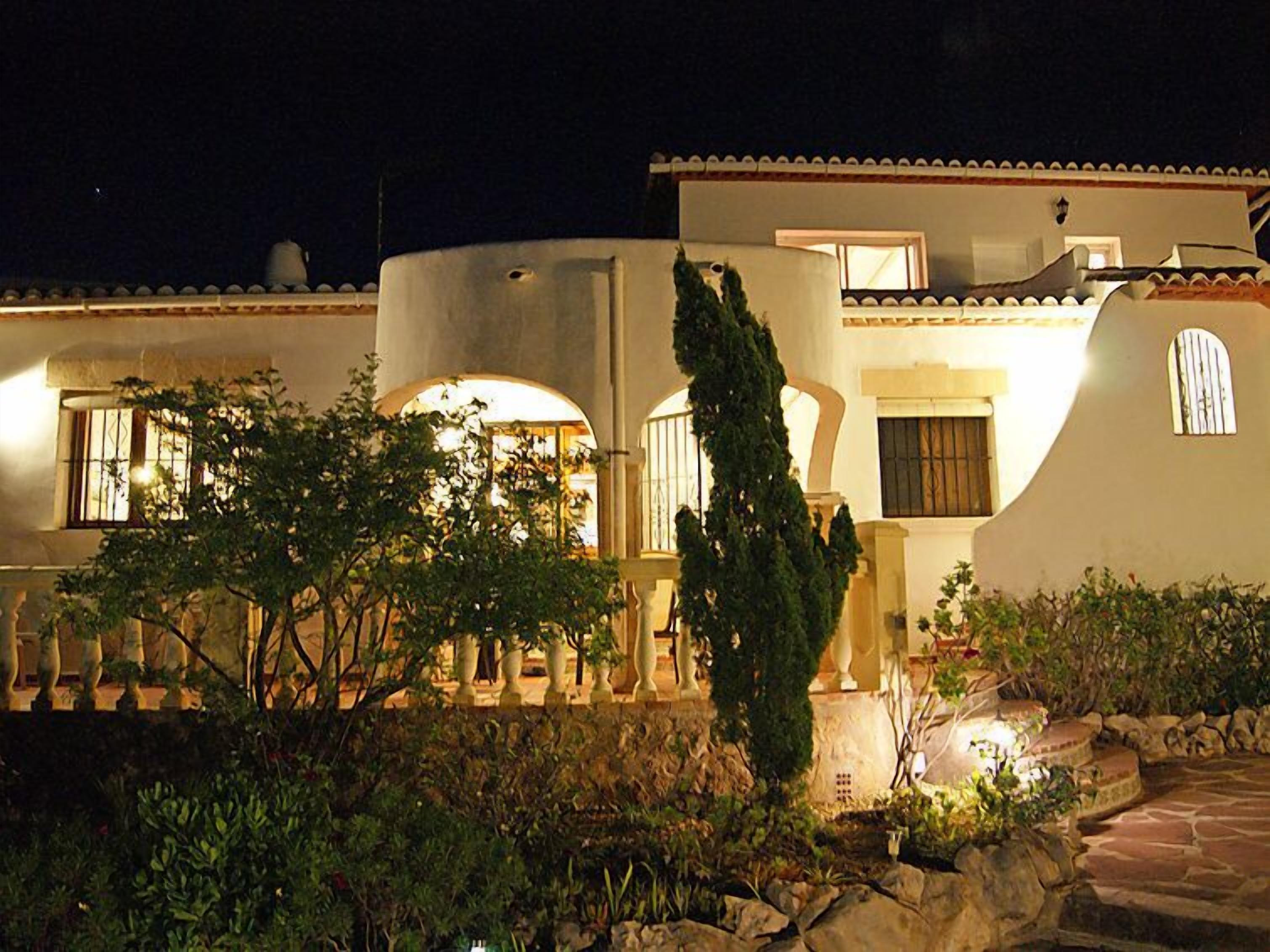 Un edificio bien iluminado con fachada curva, ventanas arqueadas y un camino de piedra que lleva a la entrada.