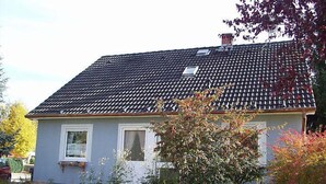 Une maison de plain-pied avec un toit recouvert de tuiles sombres, des murs extérieurs blancs et un petit porche à l’avant.