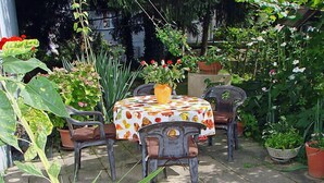 Une terrasse avec une table ronde recouverte d’une nappe à motifs de fruits, entourée de chaises.