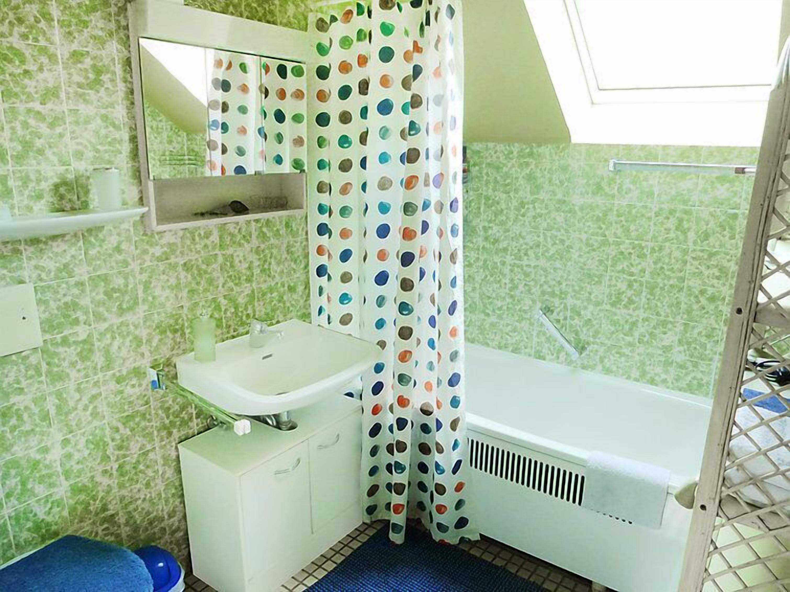 Een badkamer met een witte wastafel, een spiegel, een douchegordijn met kleurrijke stippen en een groene betegelde muur.