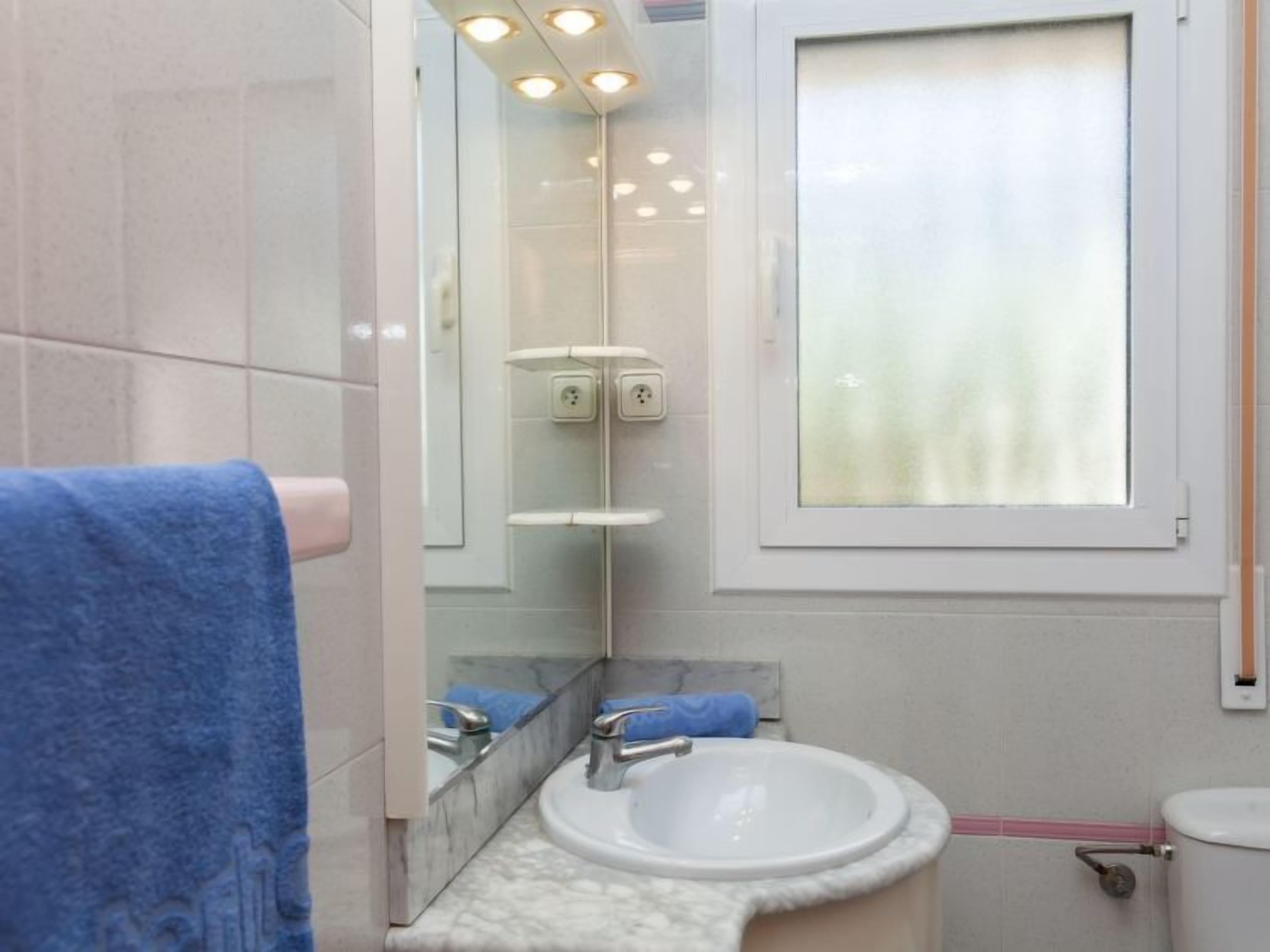 Un baño con lavamanos blanco, espejo y ventana con cortina.