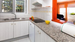 A modern kitchen with white cabinets, a granite countertop, a sink, and a window with a view of greenery. - Torre Mar by Interhome (Miami Platja)