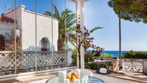 A glass table with chairs on a balcony overlooking the sea, with a view of a white building and a stone wall. - Torre Mar by Interhome (Miami Platja)