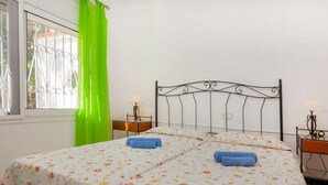 A double bed with floral bedding, two bedside tables with lamps, a window with a metal grill, and a green curtain. - Torre Mar by Interhome (Miami Platja)