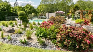Ein angelegter Garten mit Pool, einer Pergola und verschiedenen Pflanzen und Sträuchern.
