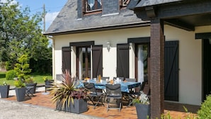 Ein zweistöckiges Haus mit einer Terrassenfläche, die einen Tisch und Stühle beherbergt, umgeben von Blumentöpfen.