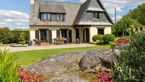 Ein zweigeschossiges Haus mit einem geneigten Dach, einer Veranda und einem gepflegten Garten mit Steinen und Pflanzen.