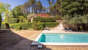 A swimming pool with a clear blue water surface, surrounded by a gravel area. There are lounge chairs and a small table near the pool. The property is surrounded by dense greenery and trees. - Les Ecureuils by Interhome (Gordes)