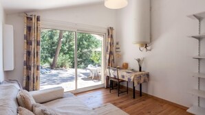 A room with a sofa, a dining table with chairs, a hanging light fixture, and a large window with curtains. - Les Ecureuils by Interhome (Gordes)
