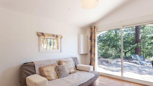 A modern living room with a sofa, a large window, and a view of a garden. - Les Ecureuils by Interhome (Gordes)