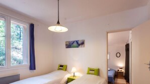 A bedroom with two beds, a window with curtains, a painting on the wall, and a hallway leading to another room. - Les Ecureuils by Interhome (Gordes)