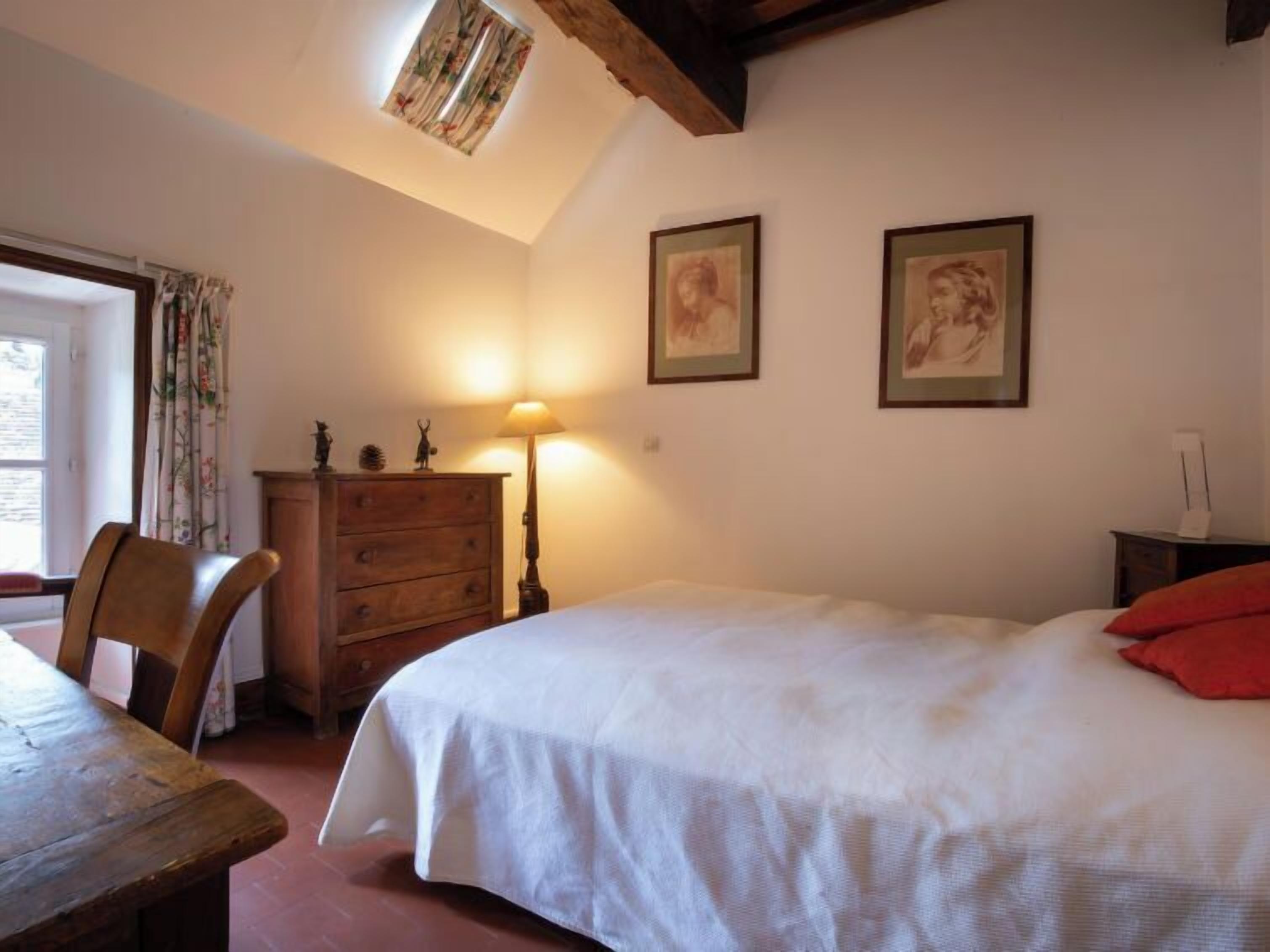 Une chambre à coucher avec un lit, une commode en bois, un bureau et une fenêtre avec des rideaux.