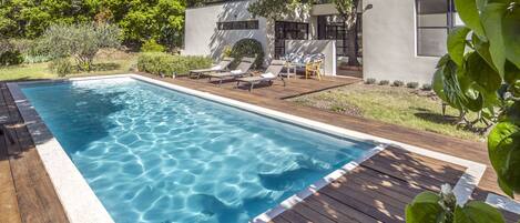 A rectangular swimming pool with clear blue water, surrounded by a wooden deck.